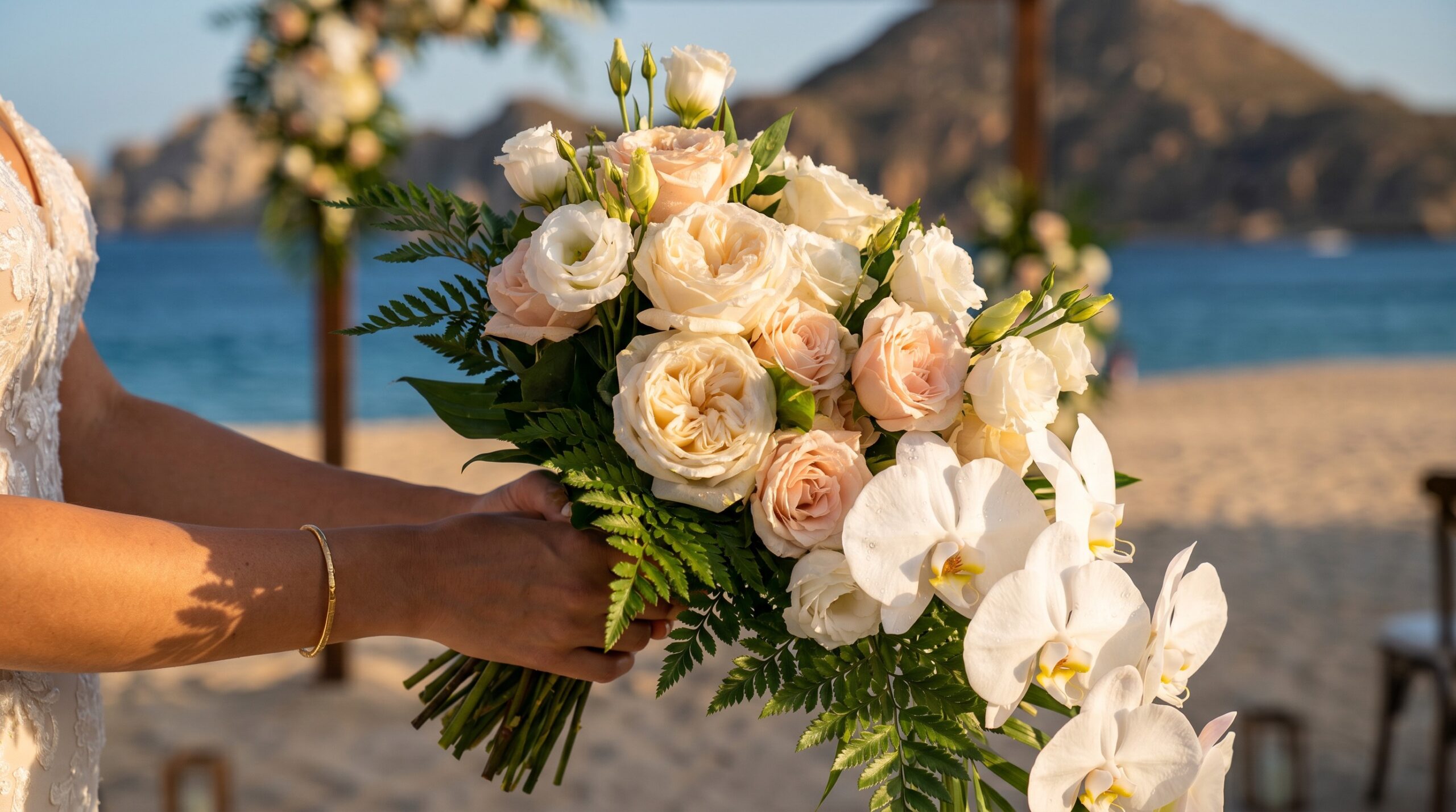 Ramo de novia con rosas garden crema, orquídeas blancas y flores tropicales contra la puesta de sol en Los Cabos